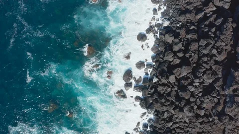 Blue ocean waves break into white foam by black stones on a shore. Aerial of Stockbeeldmateriaal 118016553