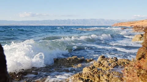 Blue ocean waves crash forcefully against a rocky coastal shore. Stock Footage 337409921