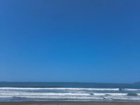 Blue ocean waves crashing on empty sandy beach under sky Stock Photos