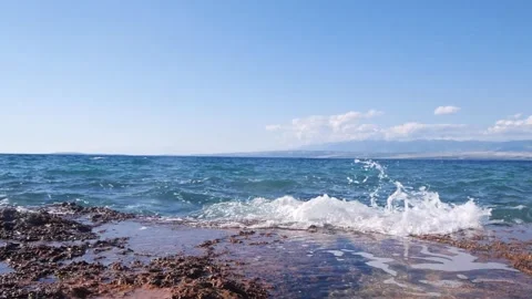 Blue ocean waves crashing gently onto a rocky coastal shore. Stock Footage 337406028