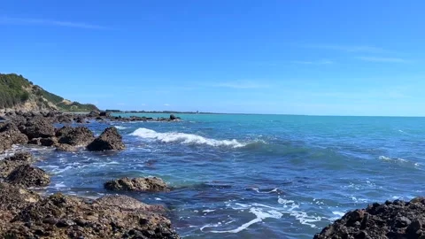 Blue ocean waves hitting rocky coastline under sunny clear sky Stock Footage 310245144