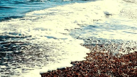 Blue ocean waves wash over a dark pebble shore Video stock 332284391