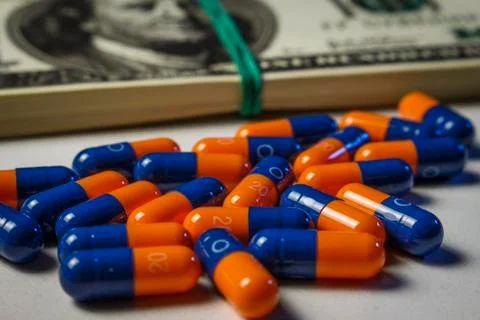 Blue-orange capsules with a pack of dollars on a white doctor's table Stock Photos