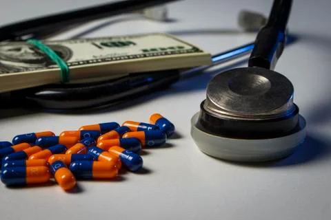 Blue-orange capsules with a pack of dollars and a phonendoscope on a white do Stock Photos