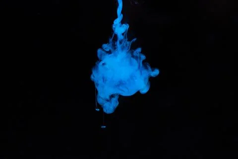 Blue paint dissolves in water on a black background. Stock Photos