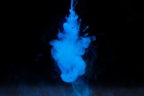 Blue paint dissolves in water on a black background. Stock Photos