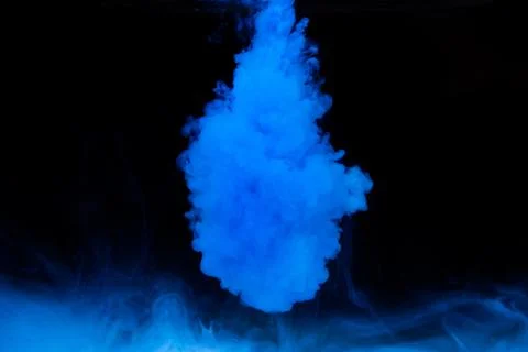 Blue paint dissolves in water on a black background. Stock Photos