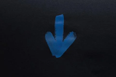 Blue painted arrow pointing down on black paper Stock Photos