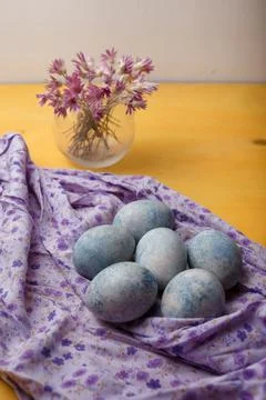 Blue painted Easter eggs on purple towel on yellow bright background. Flowers Stock Photos