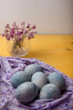 Blue painted Easter eggs on purple towel on yellow bright background. Flowers 库存照片