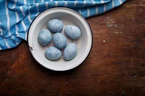 Blue painted easter eggs in white bowl, some blue striped fabric Stock Photos