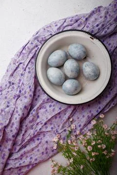 Blue painted Easter eggs in white bowl on purple kitchen table with flowers. Stock Photos
