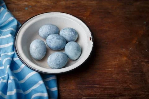 Blue painted easter eggs in white bowl, some blue striped fabric on brown Stock Photos
