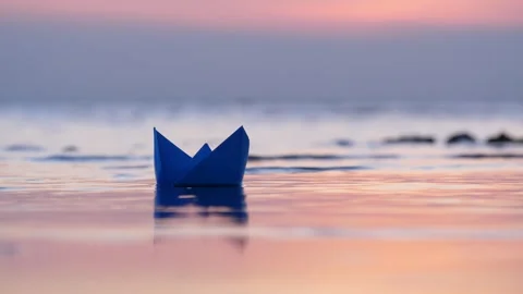 Blue paper boat stuck stranded near sea shore, sunset hour, telephoto view Stock Footage 314251324