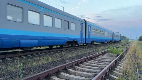 Blue passenger train moving away on railway tracks with freight cars in bac.. Stock Footage 340244978