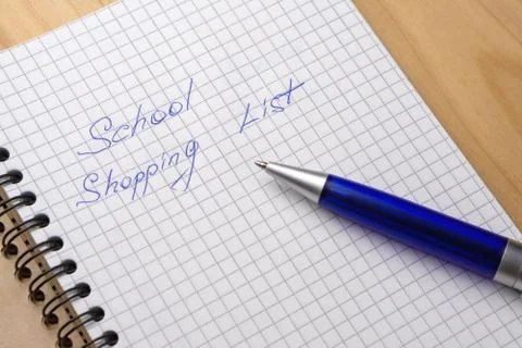 Blue pen on a notebook with sheets in a cage. Sign - school shopping list Stock Photos