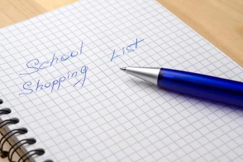 Blue pen on a notebook with sheets in a cage. Sign - school shopping list Stock Photos