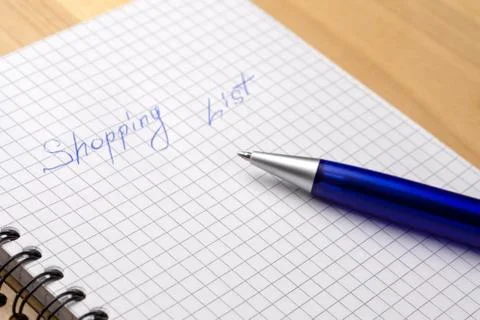 Blue pen on a notebook with sheets in a cage. Sign Shopping List. Close-up Stock Photos