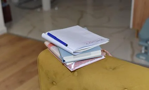 Blue pen rests on open notebook with "HOMEWORK" on stacked books on yellow Foto stock