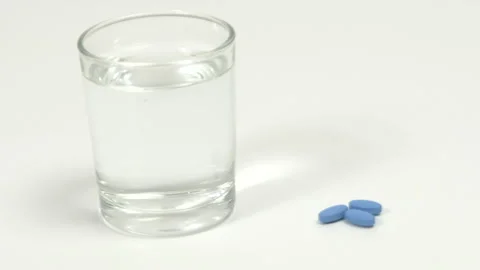 Blue pills for erectile dysfunction on white table with glass of water. Stock Footage 274035312