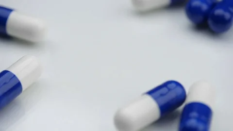Blue pills falling on white surface. Video stock 77381962