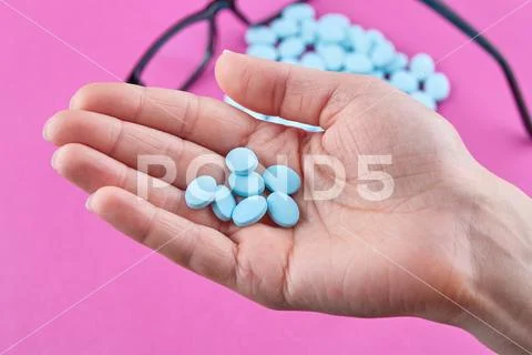 Blue pills in hand and glasses on pink background Stock Photos