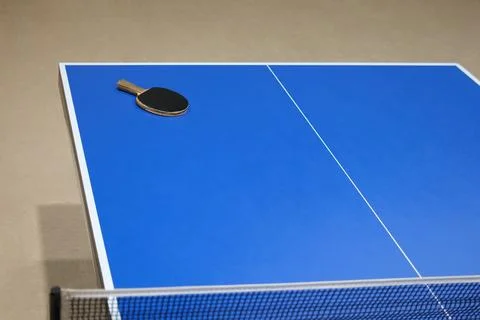A blue ping pong table with a net and a racket Stock Photos