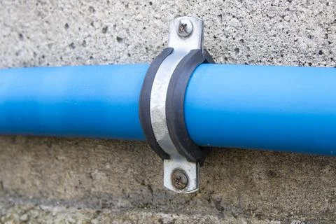 Blue Pipe Secured to Concrete Wall with Metal Clamp Stock Photos