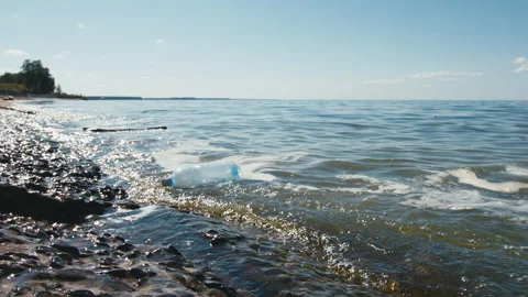 Blue plastic bottle floats on waves near sea shore, water pollution Stock Footage 210474380