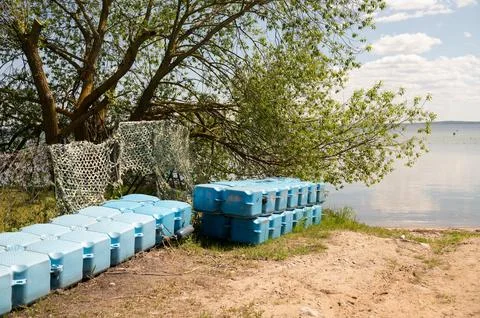 Blue plastic container stack by lake shoreline with greenery Foto stock