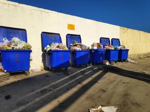 Blue plastic dumpsters with garbage stand against the wall Stock Photos