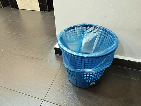 Blue plastic dustbin with a blue plastic liner, placed on a tiled floor Stock Photos
