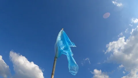 Blue plastic flag blowing in the wind on the blue sky with clouds background. Stock Footage 122311102
