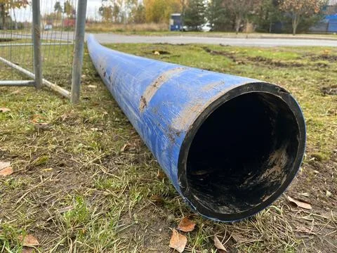 Blue plastic pipe lying on the ground, surrounded by grass and dirt, showcasing Stock Photos