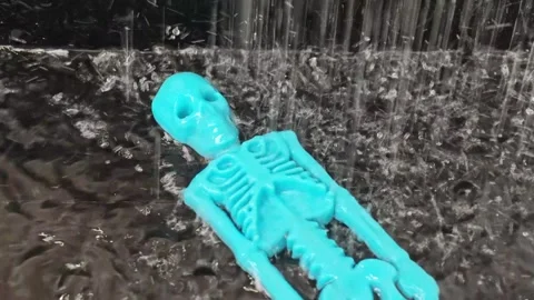 Blue plastic skeleton figure lying on wet surface as water cascades down Stock Footage 338172550