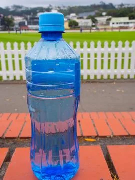 Blue plastic water bottle on brick bench near sports field Фото