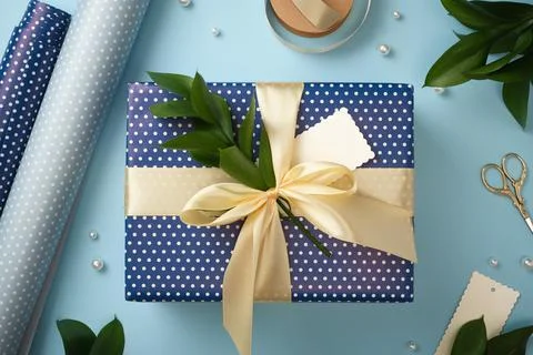 Blue polka dot gift box with a large cream ribbon bow and green twig, surroun Stock Photos