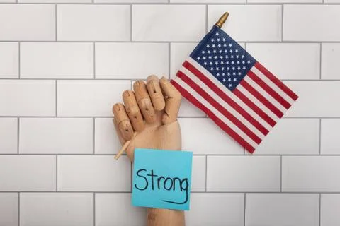 Blue post note with word Strong on wooden hand holding USA flag Stock Photos