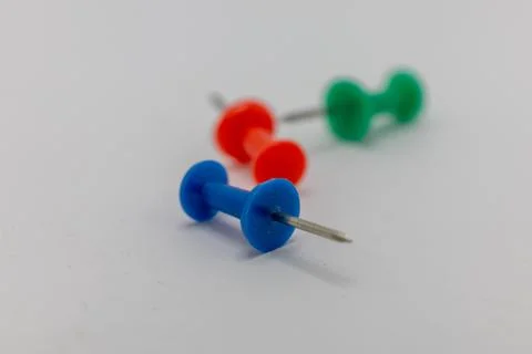 A blue pushpin is in focus in the foreground, with blurred red and green push Stock Photos