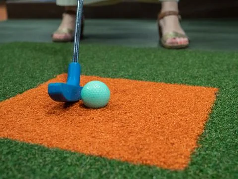 Blue putter on turf lined up next to green golf ball on miniature golf course Stock Photos