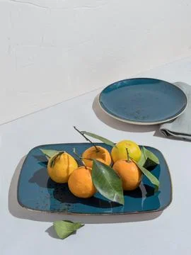 Blue rectangular plate of sweet tangerines with leaves on table Stock Photos