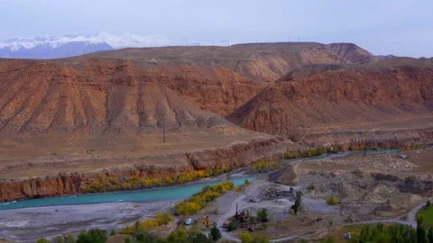 A blue river flows by the mountains and a snow-white mountains in the distance Stock Footage 166160012