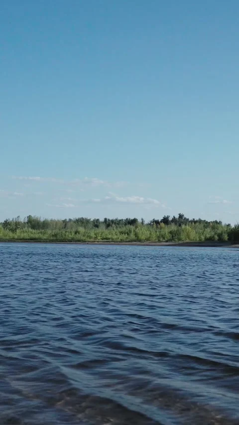 Blue river water with small waves and distant green bank under blue sky Stock Footage 346640870