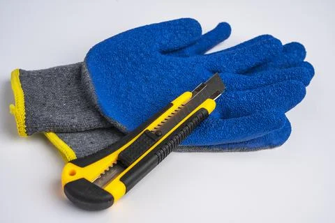 Blue rubberized work gloves and a stationery knife lie on a white background Stock Photos