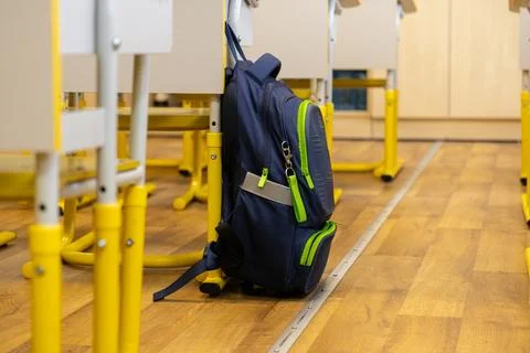 A blue schoolbag hangs on a chair in an empty primary school classroom, con.. Stock Photos