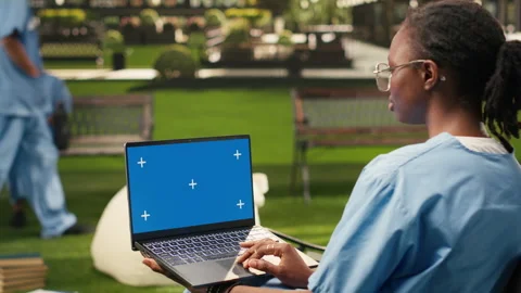 Blue screen mockup on laptop held by seated student in scrubs on campus Stock Footage 340961432