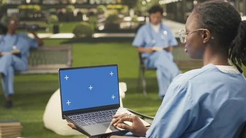 Blue screen mockup on laptop held by seated student in scrubs on campus Stock Photos