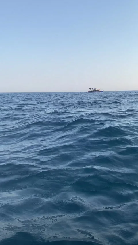 Blue sea waves ripple gently in the foreground with motorboat on the horizon Vídeos de archivo 343790344