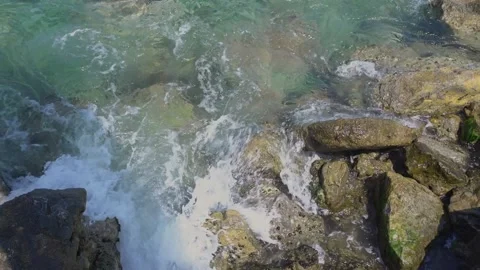 Blue sea waves with small white foam among wet brown rocks Stock Footage 157287900