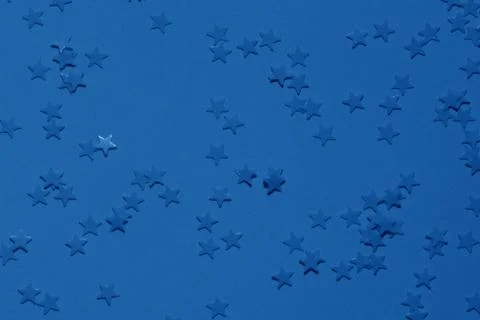 Blue sequins on a bright blue background with confetti as asterisks. Stock Photos
